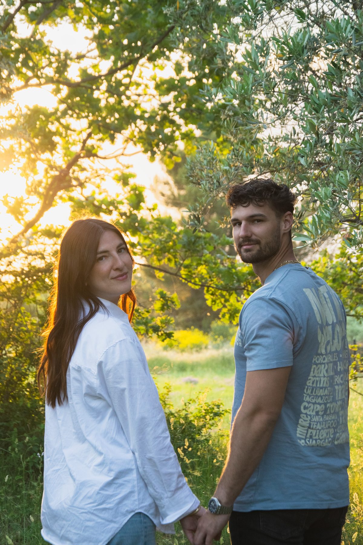 Couple main dans la main sous les oliviers se retournant vers l’objectif